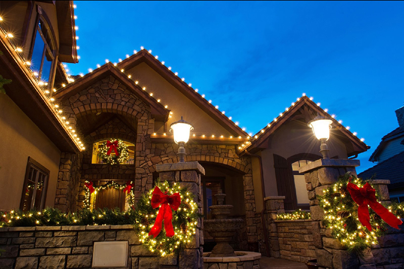 stone and stucco home with holiday lighting, bows and garlands